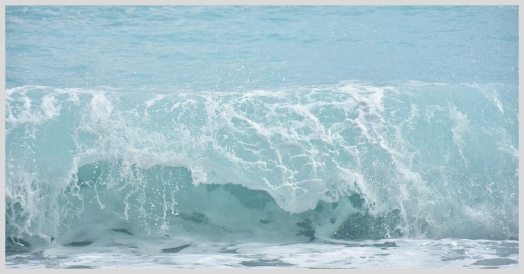A wave crashing on the shore of Gili Island, with clear blue water and sandy beach in the background.